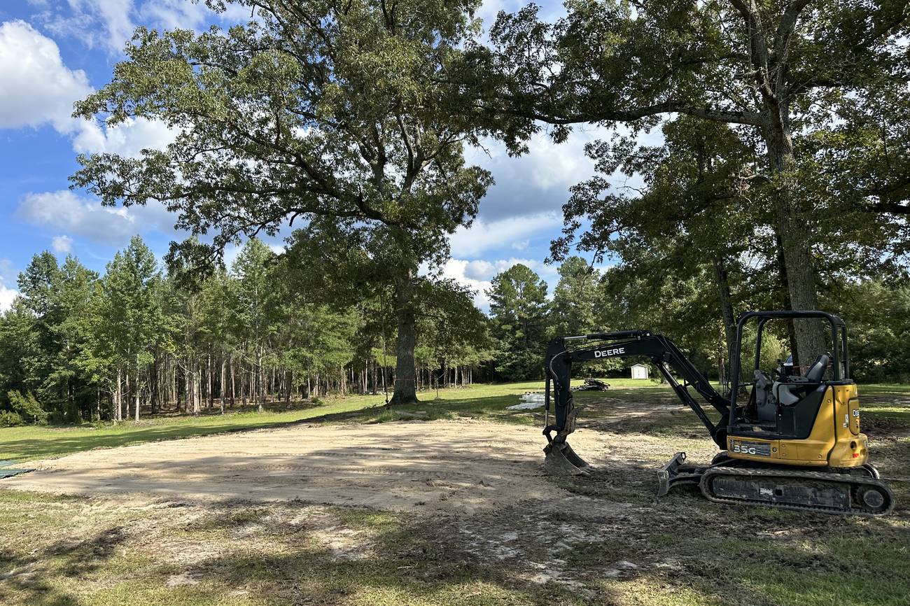 Excavator working a cleared lot beneath large live oaks