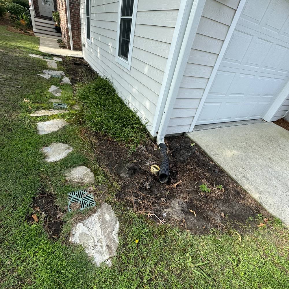 Drain outlet and grate installed at the corner of a house foundation
