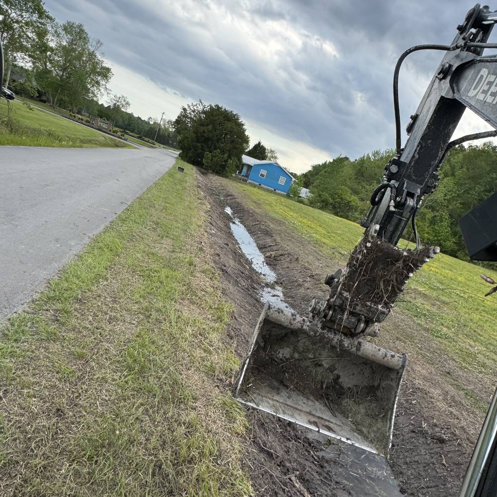 Excavator cutting a drainage swale beside a road