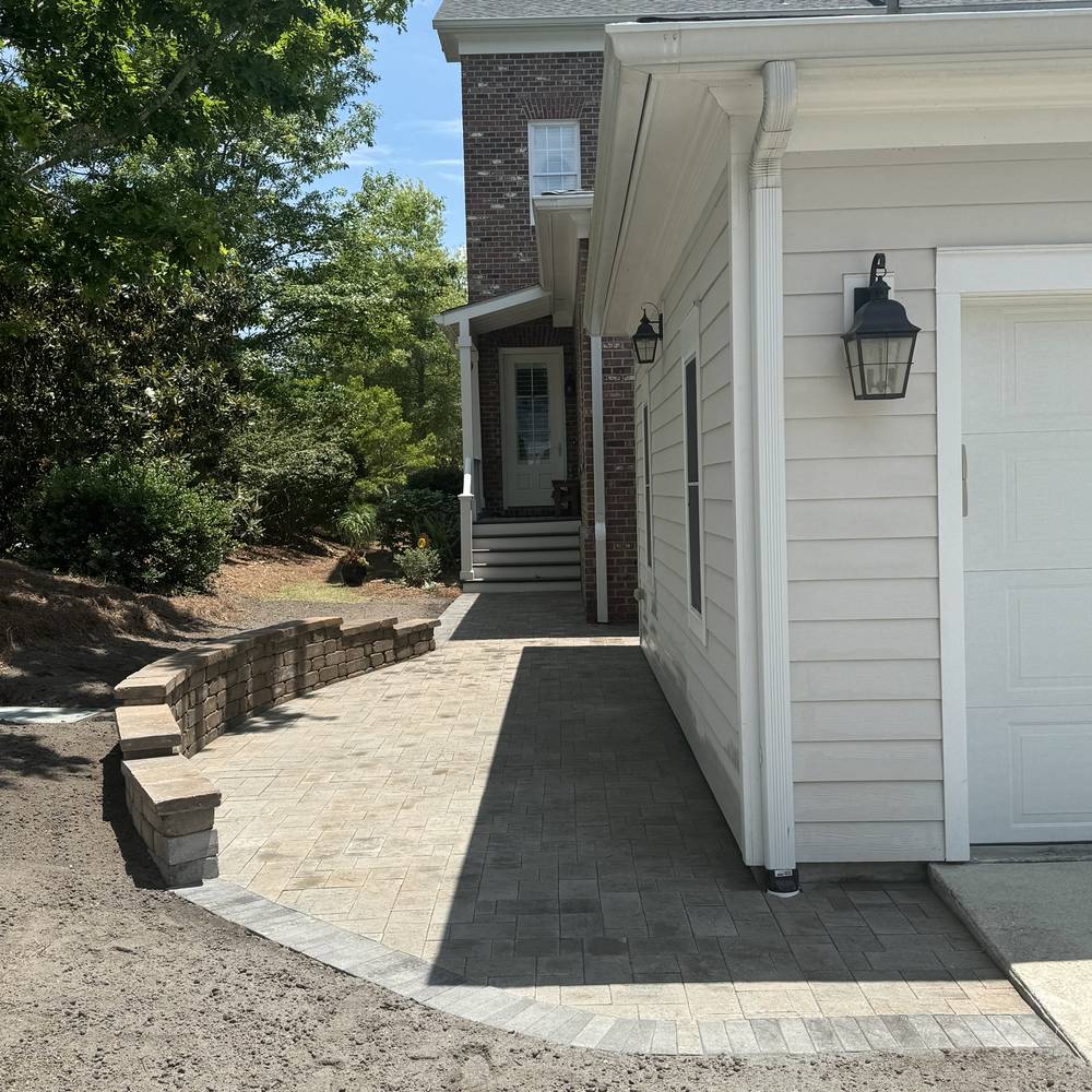 Paver walkway running alongside a house against a retaining wall