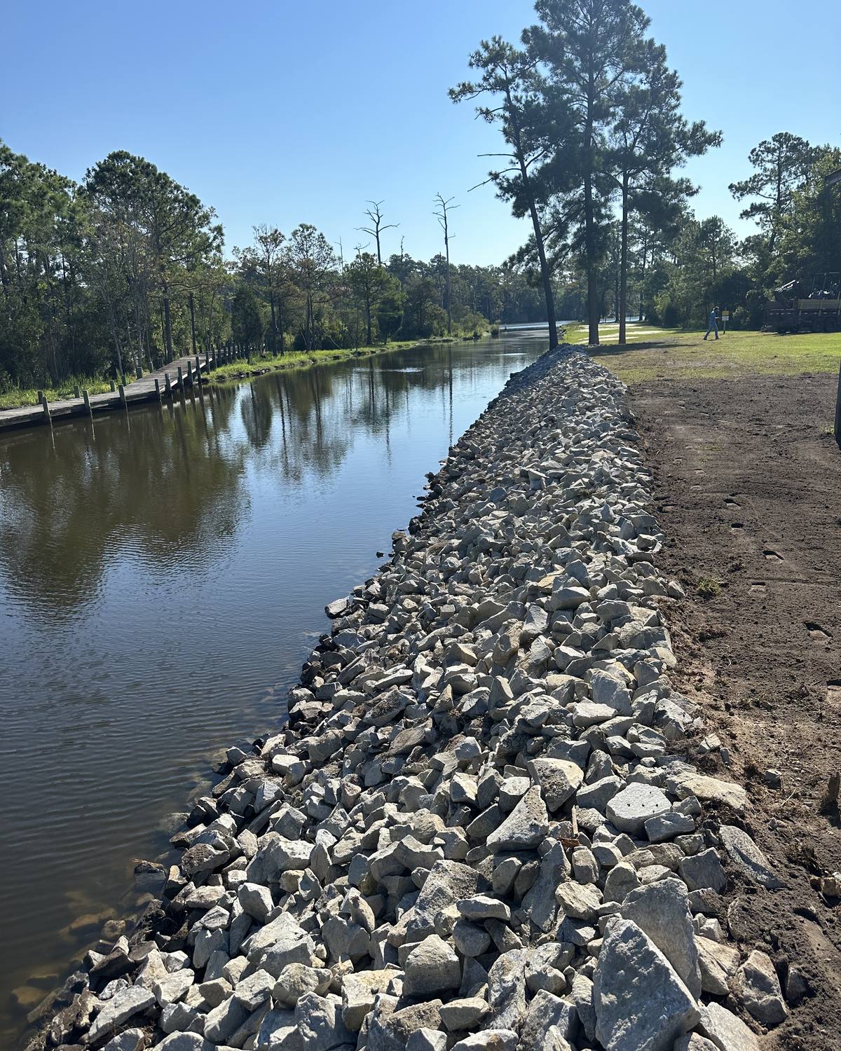The same canal bank after: armored with riprap stone along the full length